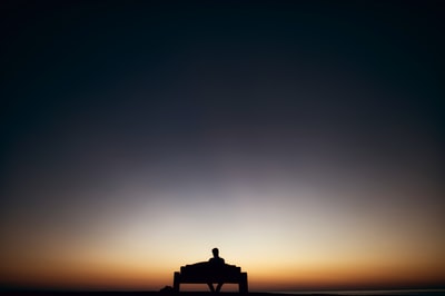 人坐在长椅上面临日落
